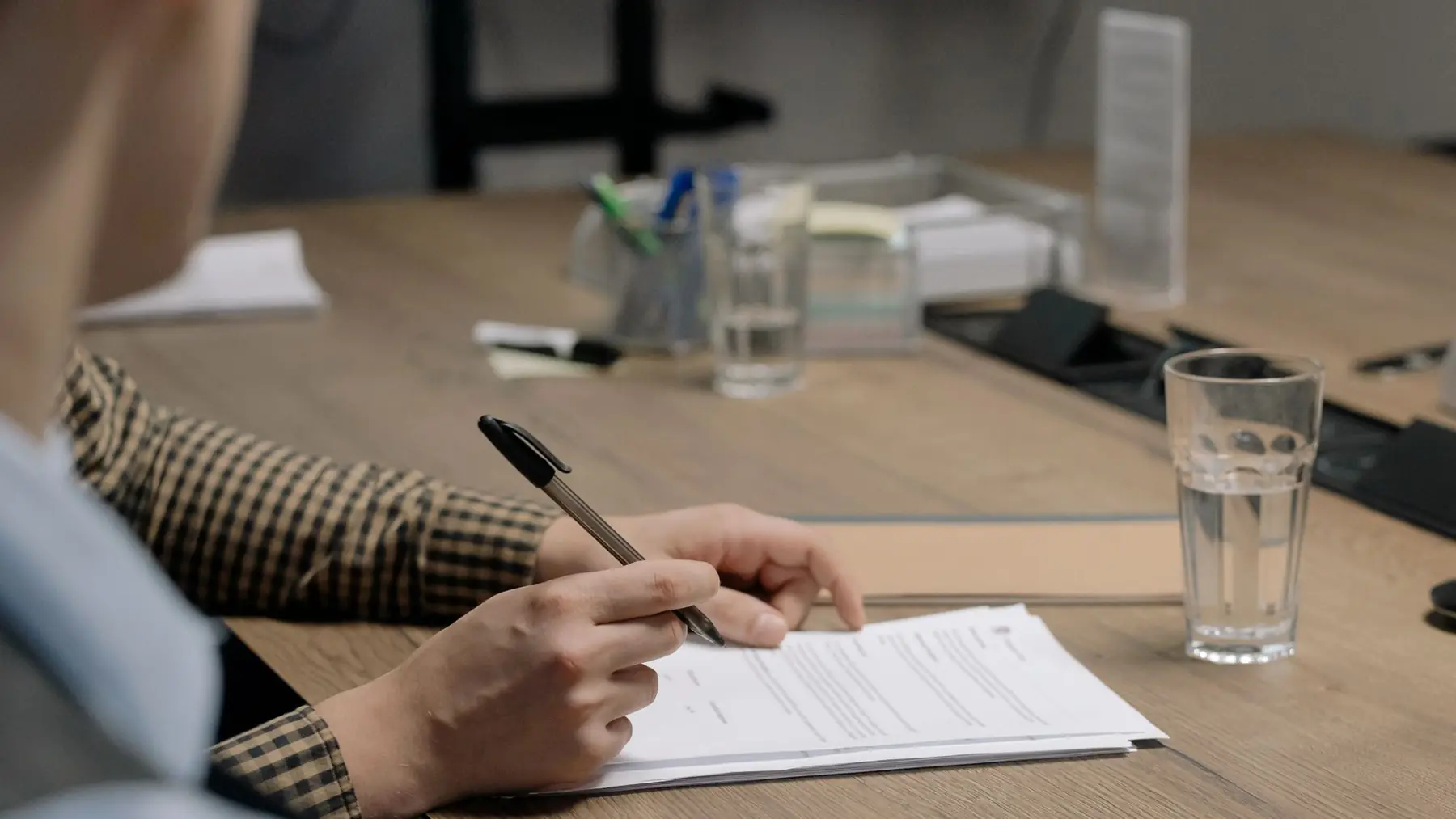 Persona firmando unos documentos sobre una mesa de madera