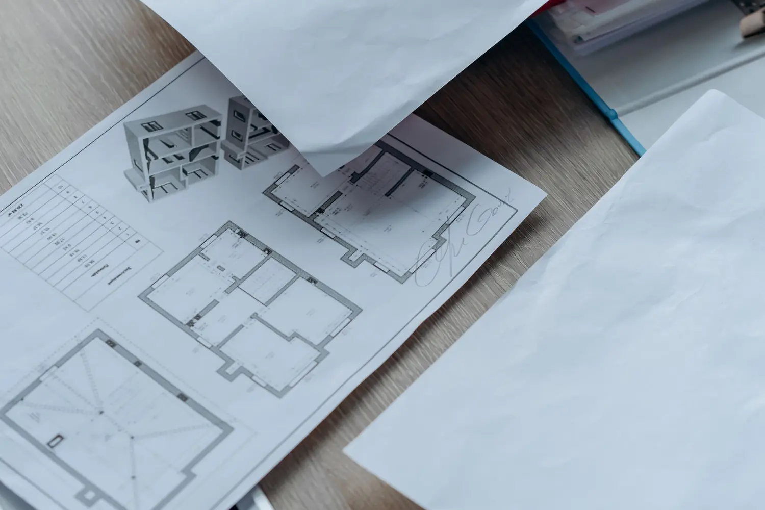 Planos de una vivienda y documentación extendidos sobre una mesa de madera